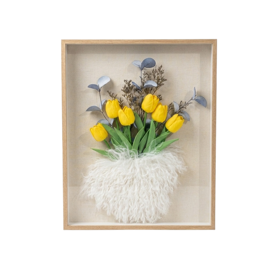 A framed floral wall art piece featuring yellow tulips with green leaves, blue-gray foliage, and a fluffy white textured base inside a light wood shadow box on a white background.