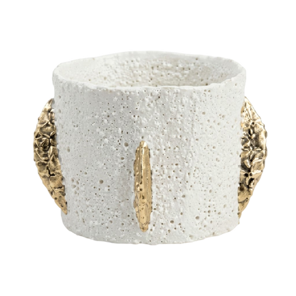 A textured white ceramic cuff bracelet with gold leaf accents on the front and sides, set against a plain white background.
