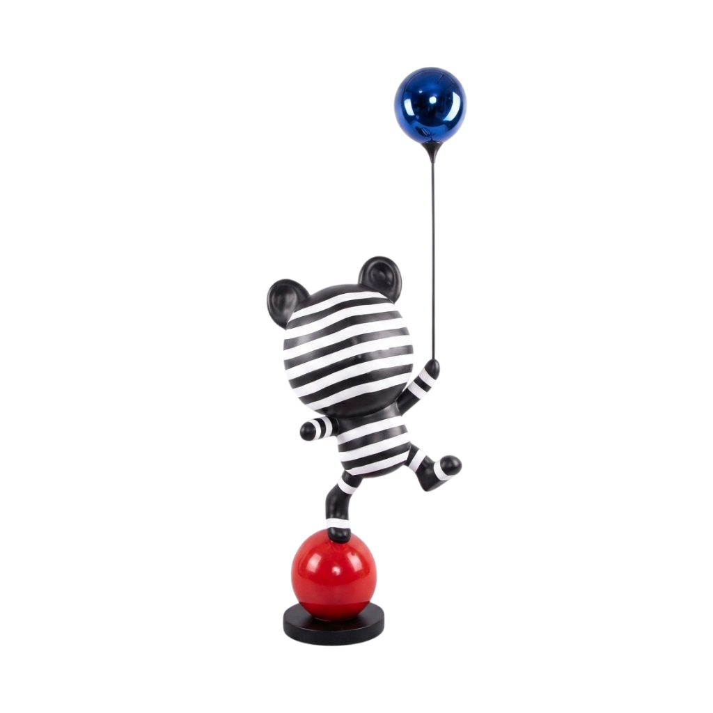 A stylized zebra figurine balancing on a red ball, holding a blue balloon, against a plain white background.