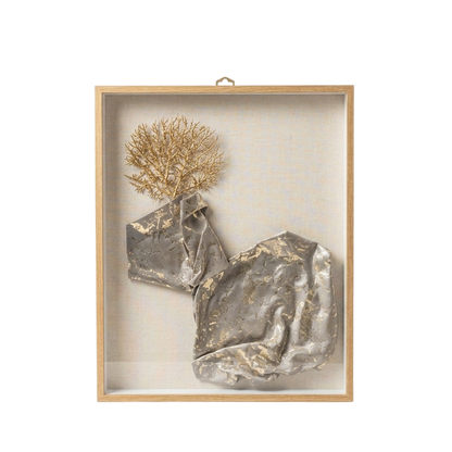 A framed abstract wall art piece with a light wood frame and clear glass cover, featuring crumpled metallic silver forms and a dried gold botanical element on a neutral off-white background.